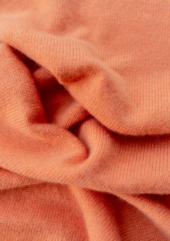 Close-up detail of Merino Triangle Scarf in Apricot showing soft, textured knit fabric with gentle folds and ripples highlighting the luxurious merino wool texture in a warm apricot color shade